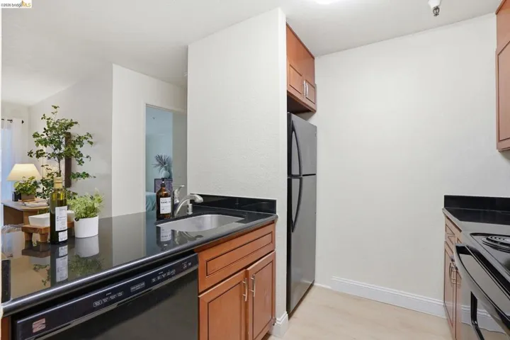Kitchen featuring dark countertops, wood cabinetry, a stainless steel refrigerator, and a built-in dishwasher