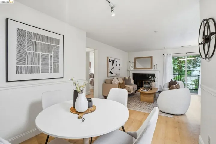 Open-concept living space featuring wood-finish flooring, a white-painted fireplace mantel, and sliding glass doors opening to an exterior balcony