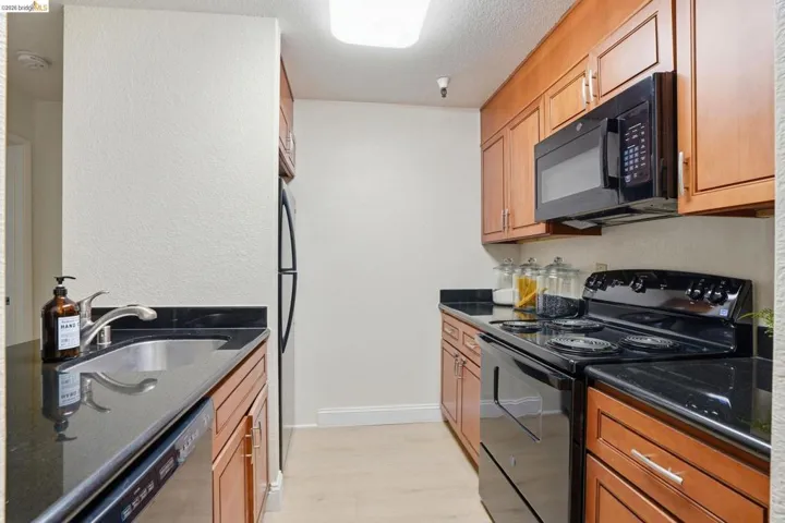 Galley kitchen featuring wood-finish cabinetry, black countertops, and light wood-finish flooring
