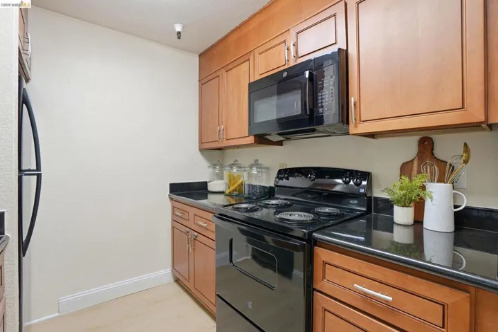Kitchen featuring wood cabinetry, black appliances, dark countertops, and wood-finish flooring
