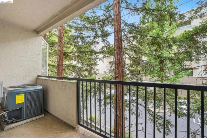 Balcony featuring a stucco exterior, black metal railing, and mature trees providing natural screening