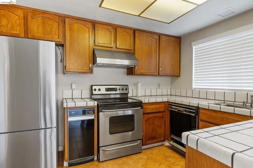 Kitchen with tile countertops, stainless steel appliances, wood finish cabinets, and light tile patterned flooring