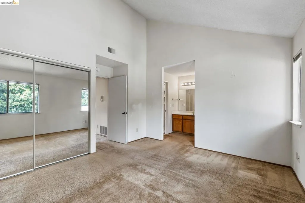 Unfurnished bedroom featuring light colored carpet, a closet, ensuite bathroom, and a high textured ceiling