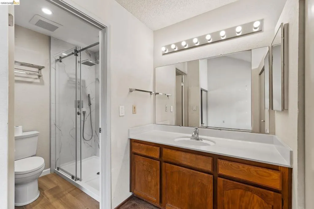 Full bath featuring vanity, a marble finish shower, and dark wood-style floors