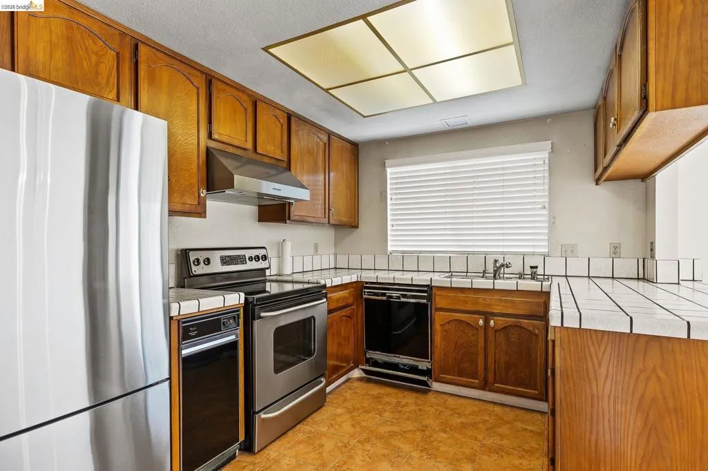 Kitchen featuring tile counters, stainless steel appliances, wood finish cabinets, and a textured ceiling