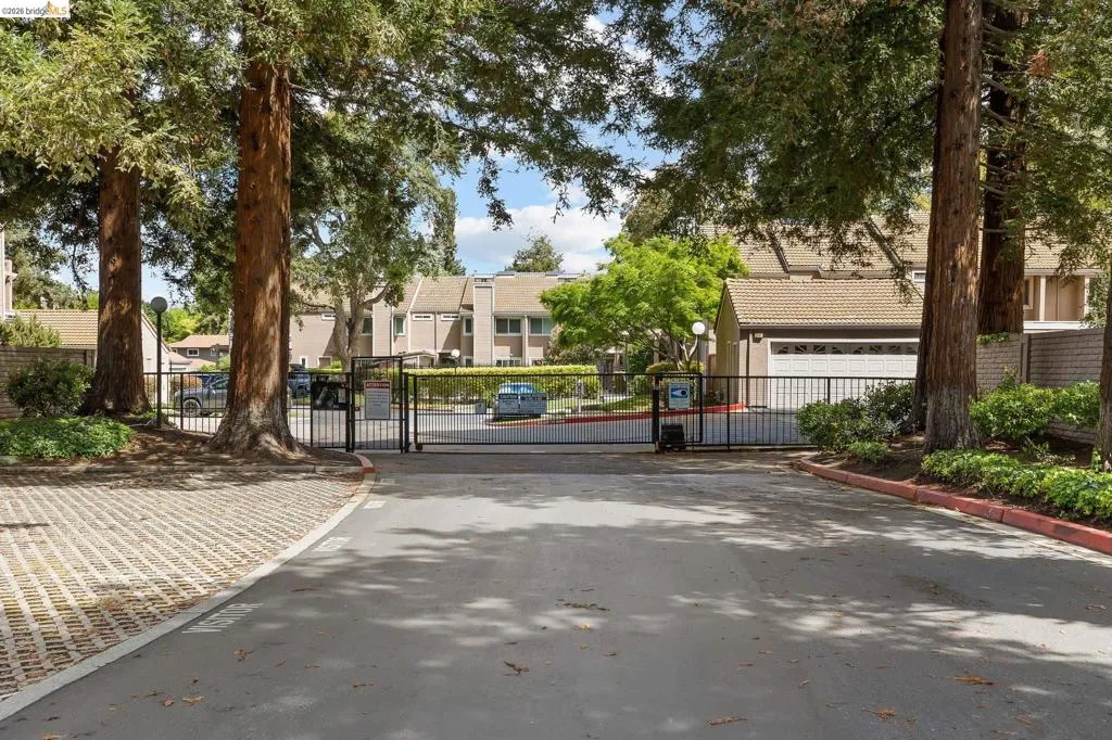View of asphalt street featuring a gated entry, a gate, curbs, and a residential view