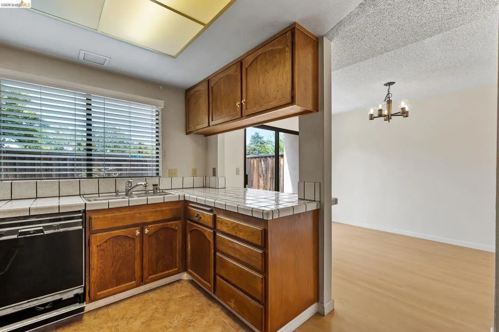 Kitchen with tile countertops, wood finish cabinets, black dishwasher, a peninsula, and hanging lights