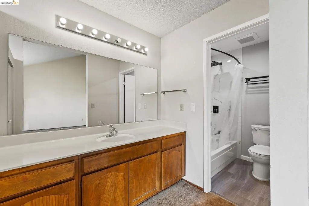 Full bath with vanity, shower / bath combo, a textured ceiling, and light wood-type flooring