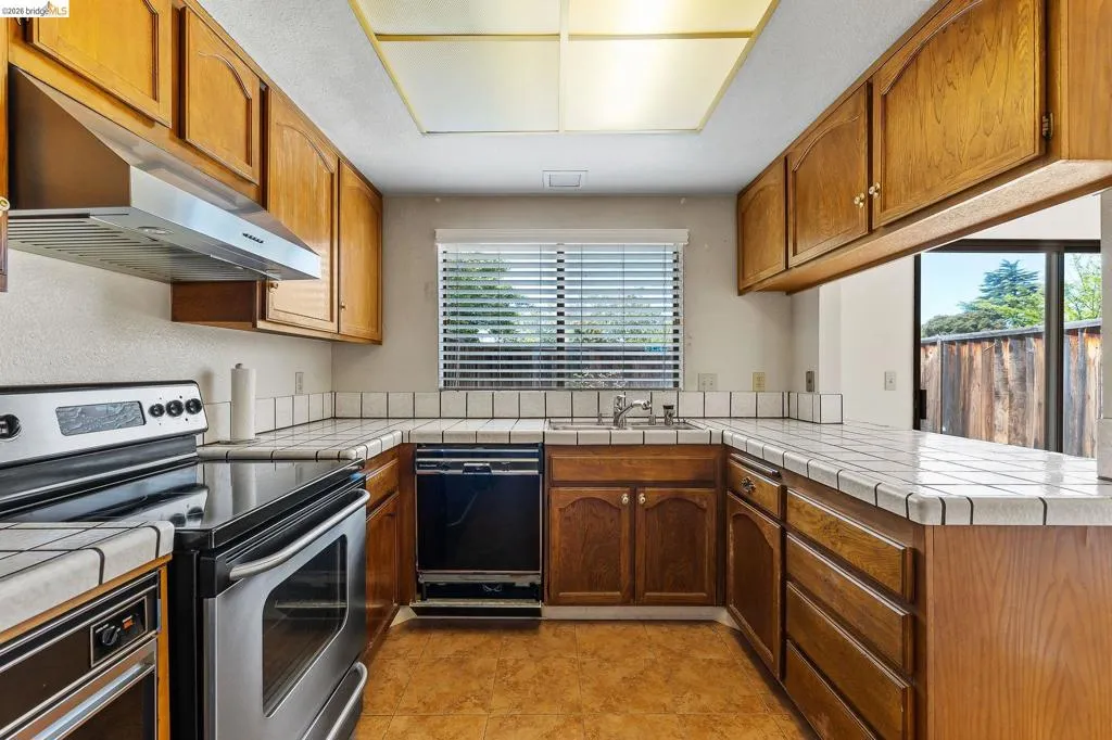 Kitchen featuring tile counters, stainless steel electric stove, a peninsula, and black dishwasher