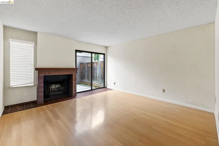 Unfurnished living room featuring a tiled fireplace, a textured ceiling, and wood finished floors