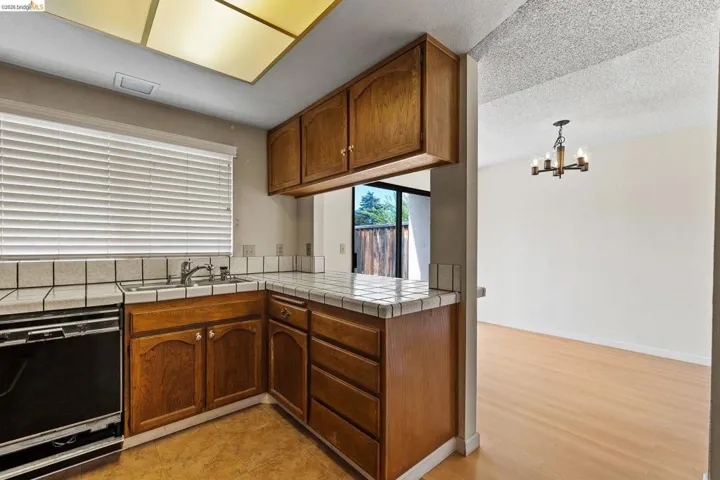 Kitchen with tile countertops, black dishwasher, wood finish cabinetry, a chandelier, and a peninsula