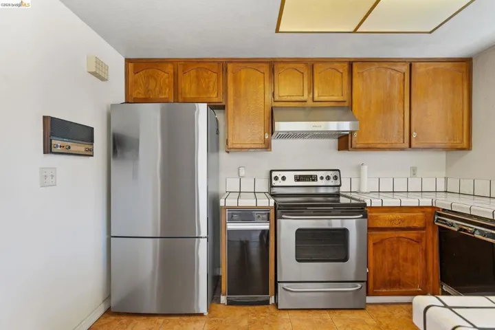 Kitchen with tile countertops, stainless steel appliances, wood finish cabinetry, and light tile patterned floors