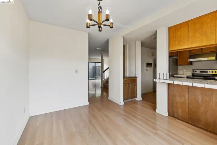 Kitchen with wood finish cabinetry, tile countertops, stainless steel appliances, light wood finished floors, and suspended lighting