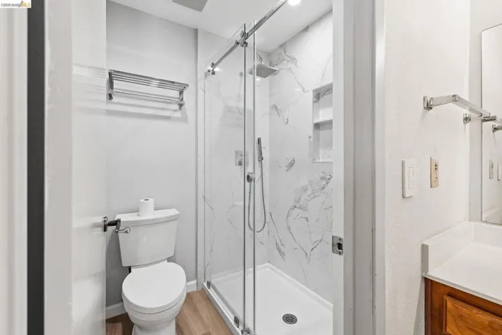 Full bath with vanity, a marble finish shower, and light wood-type flooring