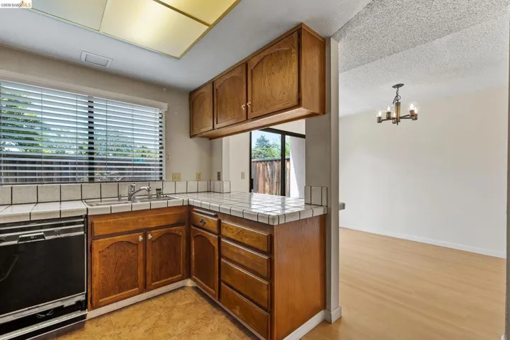 Kitchen with tile countertops, wood finish cabinets, black dishwasher, a peninsula, and hanging lights