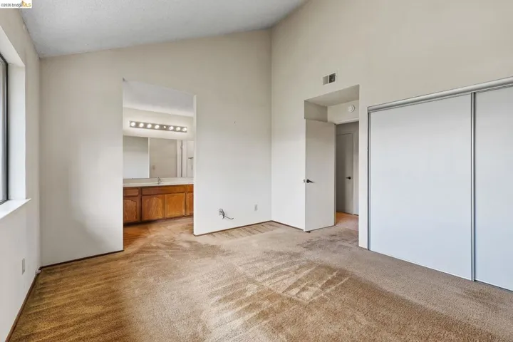 Unfurnished bedroom featuring vaulted ceiling, light carpet, and ensuite bathroom