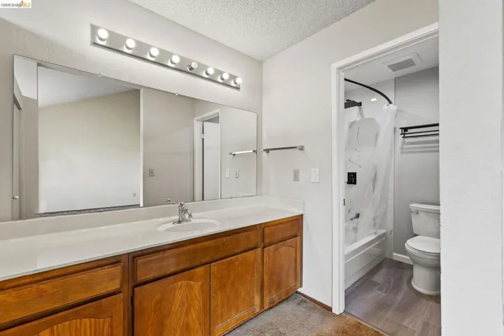 Full bath with vanity, shower / bath combo, a textured ceiling, and light wood-type flooring