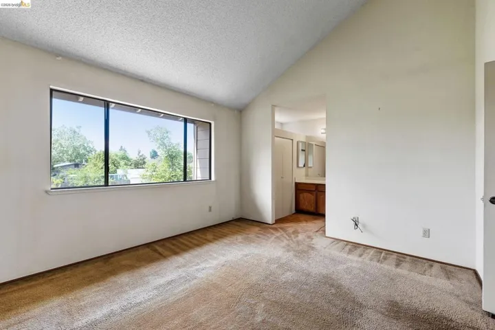 Unfurnished bedroom with a high textured ceiling, connected bathroom, and light colored carpet