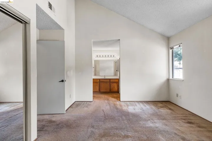 Unfurnished bedroom with a high textured ceiling, carpet flooring, and ensuite bath