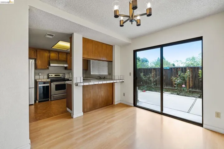 Kitchen featuring tile counters, stainless steel appliances, light wood-style floors, suspended lighting, and a textured ceiling