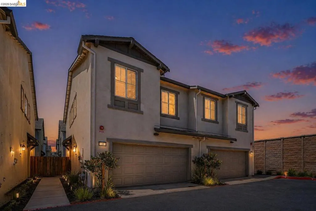 Contemporary multi-story facade featuring warm stucco, multiple gabled rooflines, two integrated garages, and illuminated entryway landscaping
