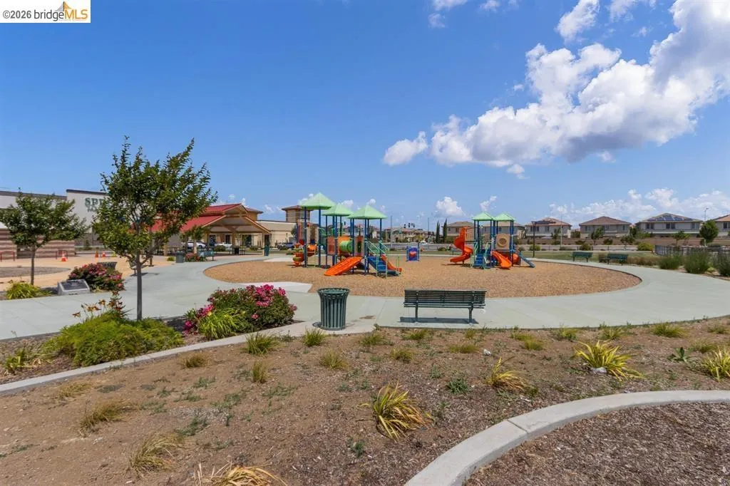 Community playground featuring multiple play structures, a wood chip surface, and surrounding concrete pathways
