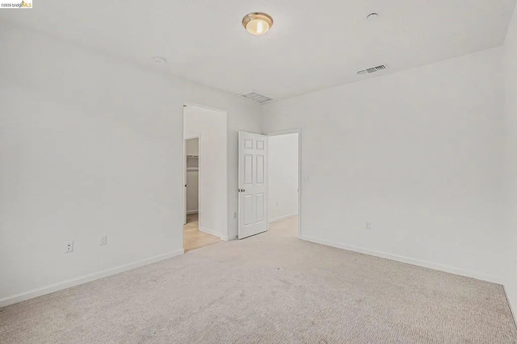 Neutral-toned carpet flooring in a spacious room, featuring white painted walls and a flush-mount ceiling light fixture