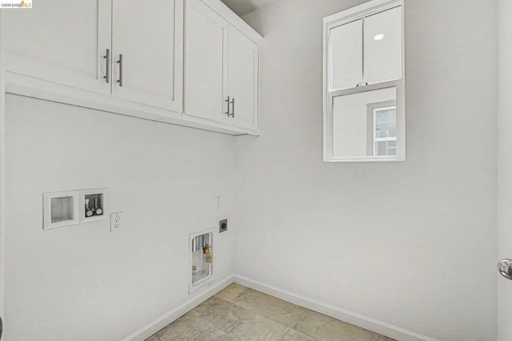 Laundry area featuring white cabinetry with brushed nickel hardware, a white-framed window, and tile flooring