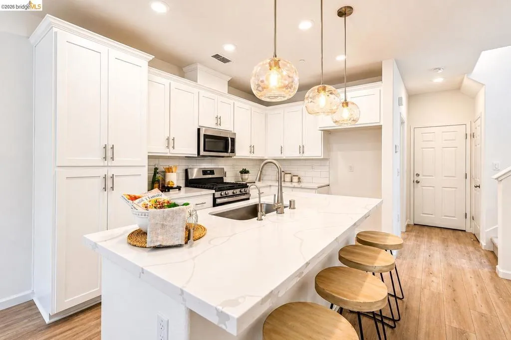 Spacious kitchen featuring an extended island with seating, white shaker cabinetry, stainless steel appliances, a subway tile backsplash, and wood-finish flooring