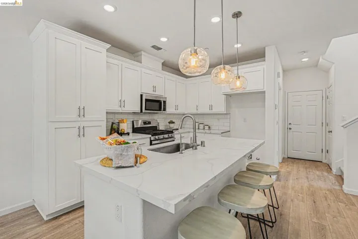 Modern kitchen featuring white shaker cabinetry, stainless steel appliances, a white subway tile backsplash, and a large island with a waterfall countertop
