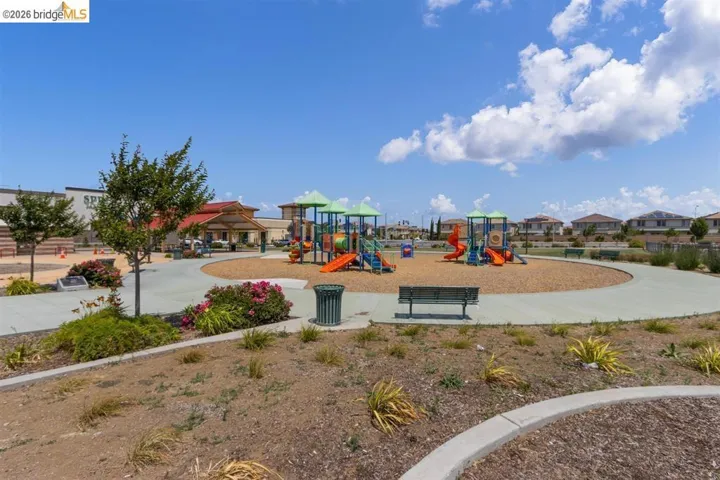 Community playground featuring multiple play structures, a wood chip surface, and surrounding concrete pathways