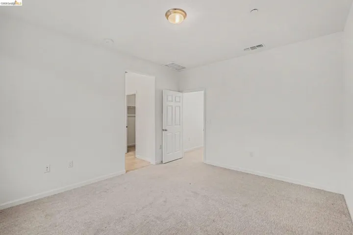 Neutral-toned carpet flooring in a spacious room, featuring white painted walls and a flush-mount ceiling light fixture