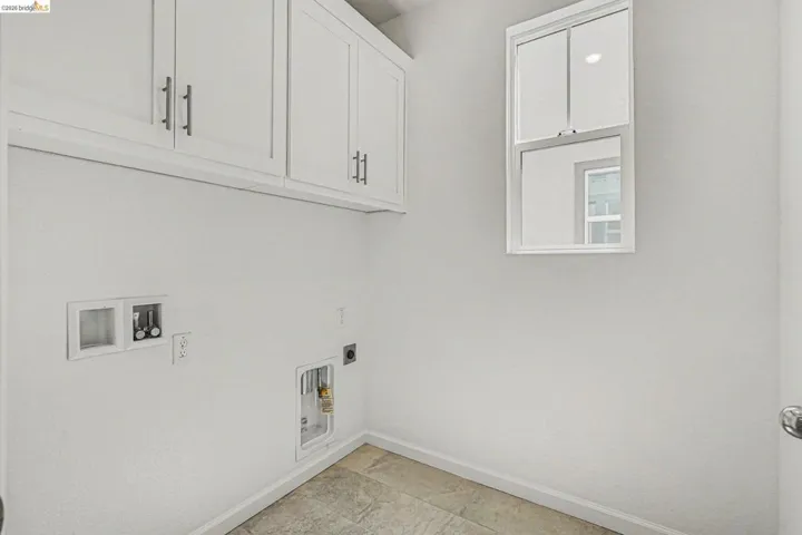 Laundry area featuring white cabinetry with brushed nickel hardware, a white-framed window, and tile flooring