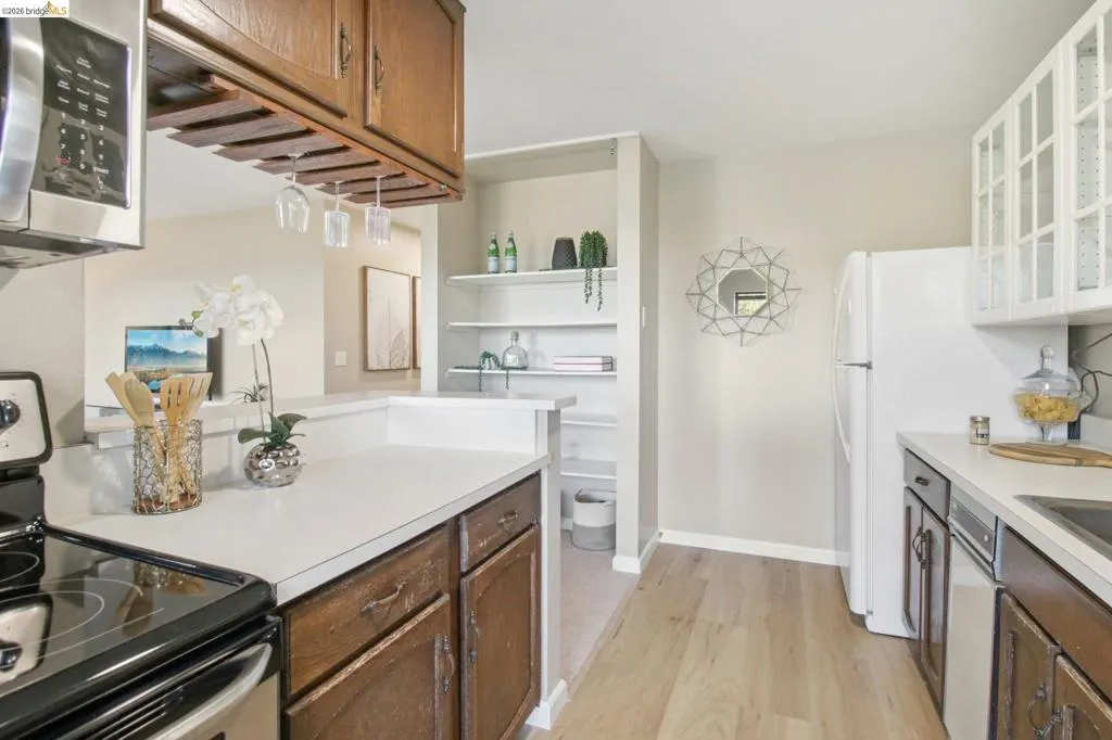 Kitchen featuring stainless steel appliances, light countertops, glass insert cabinets, light wood-style flooring, and dark wood finish cabinets
