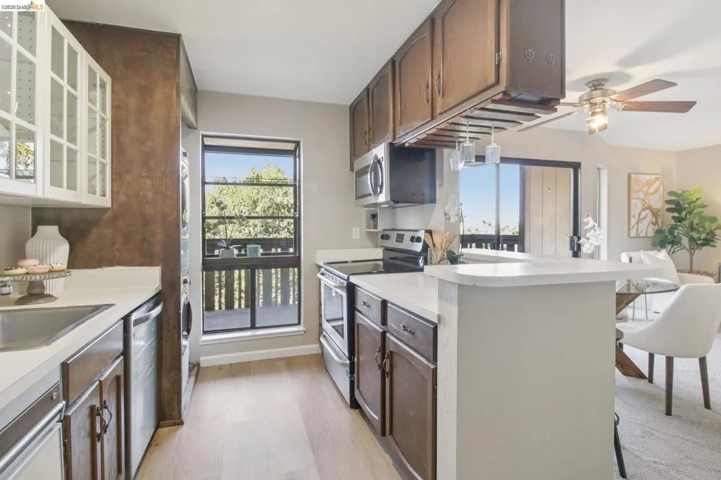 Kitchen featuring light countertops, stainless steel appliances, glass insert cabinets, a ceiling fan, and light wood-style floors