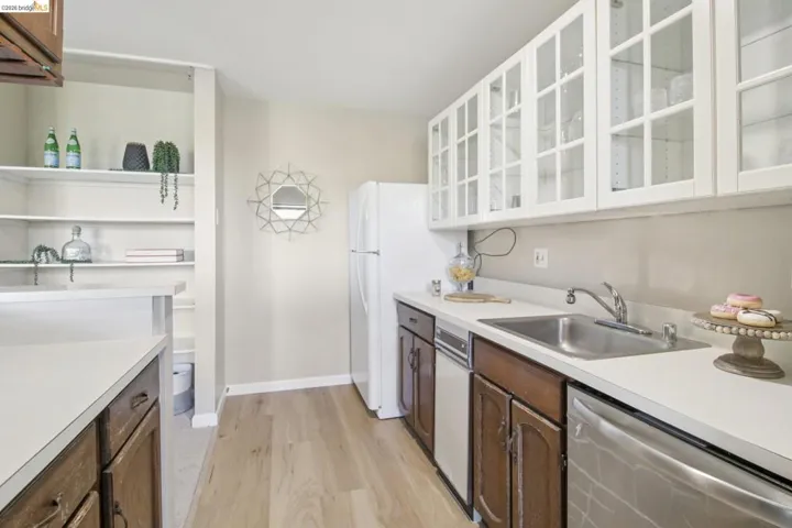 Dual tone kitchen featuring stainless steel dishwasher, light countertops, light wood-style flooring, open shelves, and glass fronted cabinets