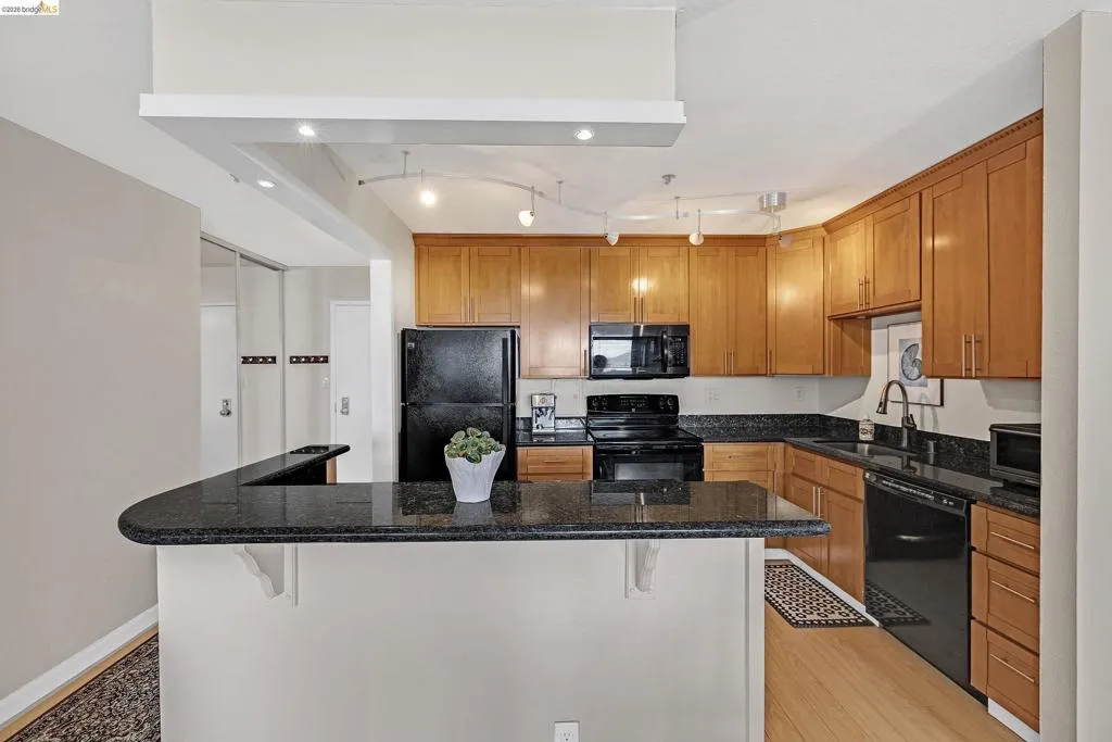 Kitchen with black appliances, a kitchen island, dark stone counters, a kitchen bar, and wood finish cabinetry