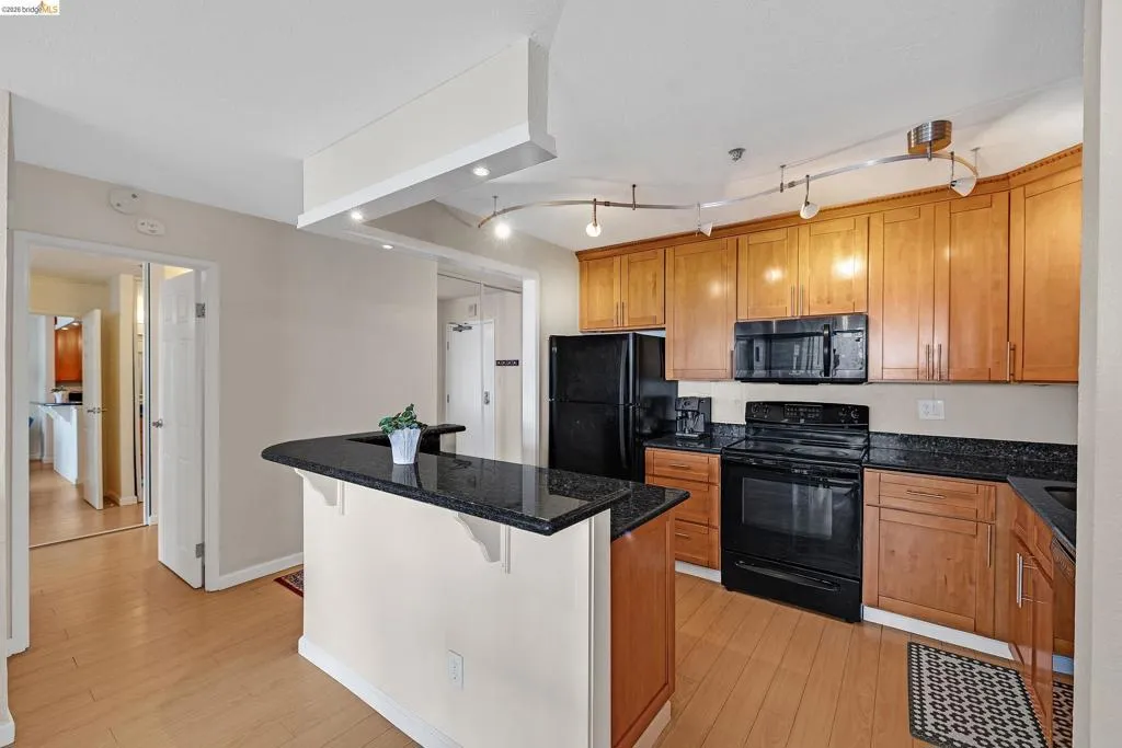Kitchen with black appliances, wood finish cabinetry, a kitchen breakfast bar, a kitchen island, and dark stone counters