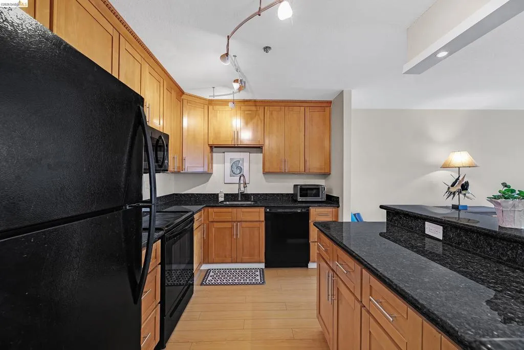 Kitchen featuring black appliances, dark stone countertops, wood finish cabinets, and light wood-type flooring