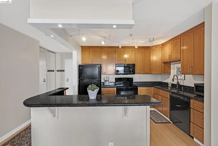 Kitchen with black appliances, a kitchen island, dark stone counters, a kitchen bar, and wood finish cabinetry