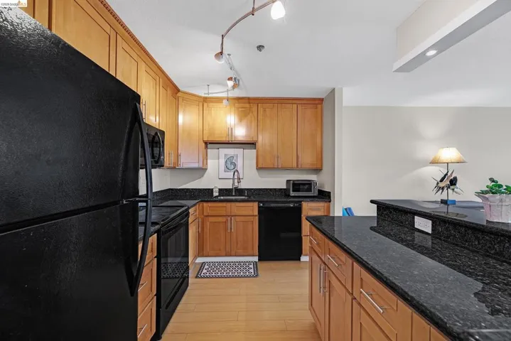 Kitchen featuring black appliances, dark stone countertops, wood finish cabinets, and light wood-type flooring