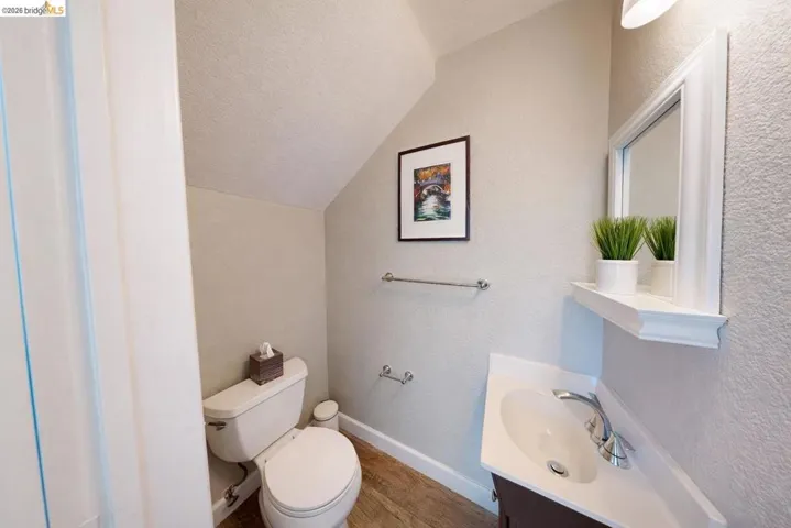 half bathroom with a textured wall, vanity, and lofted ceiling