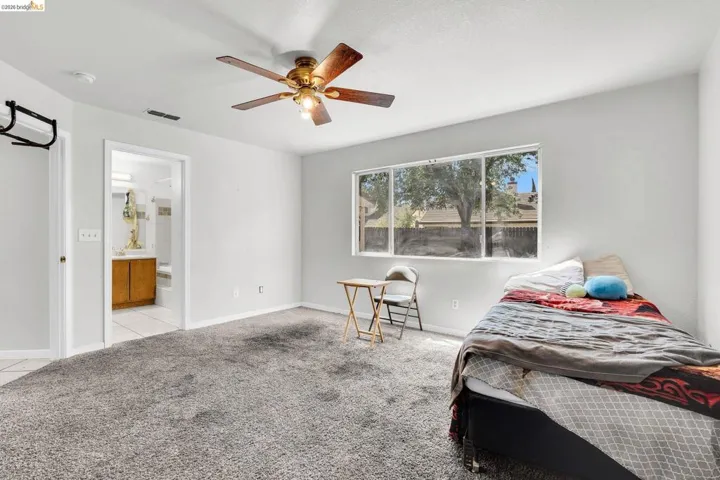 Bedroom with light colored carpet, ceiling fan, and ensuite bathroom