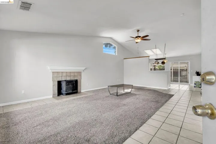 Unfurnished living room with a skylight, light tile patterned flooring, ceiling fan, vaulted ceiling, and a fireplace