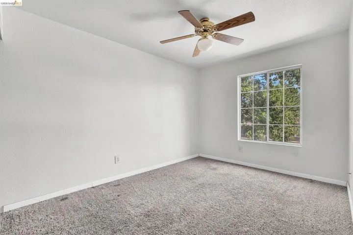 Carpeted spare room featuring ceiling fan and baseboards