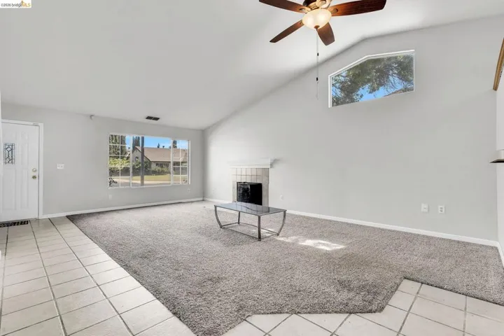 Unfurnished living room with light colored carpet, light tile patterned flooring, a tiled fireplace, vaulted ceiling, and ceiling fan