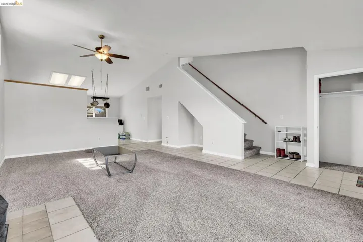 Unfurnished living room featuring light colored carpet, light tile patterned floors, a ceiling fan, vaulted ceiling, and a skylight