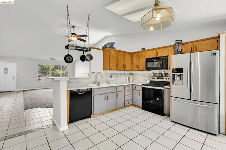 Kitchen with black appliances, light countertops, light tile patterned floors, ceiling fan, and open floor plan