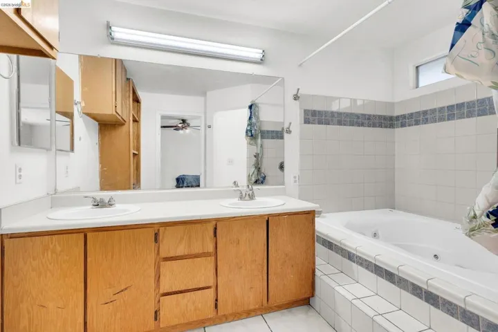 Full bath featuring double vanity, a combined bath / shower with jetted tub, and a ceiling fan