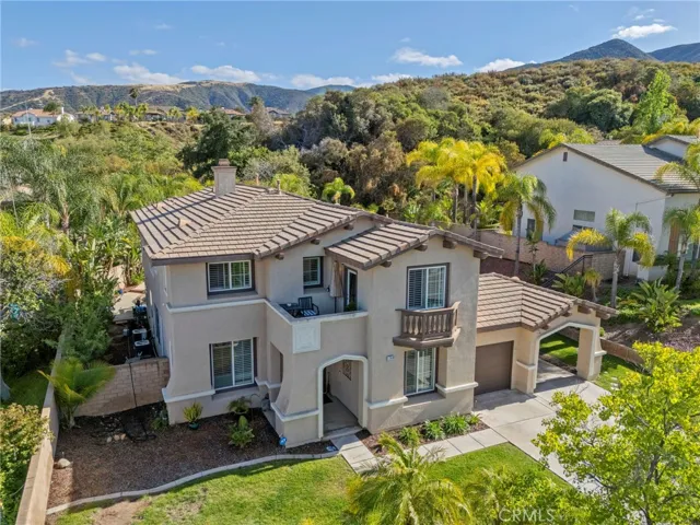 View of the home with surrounding greenery, hillside backdrop, and neighboring properties